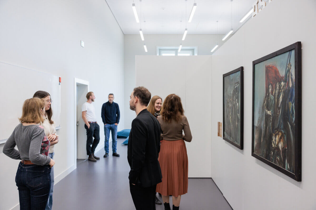 Mehrere Besucher*innen in der Pop-Up-Ausstellung. Am rechten Bildrand sieht man zwei an der Wand hängende Gemälde