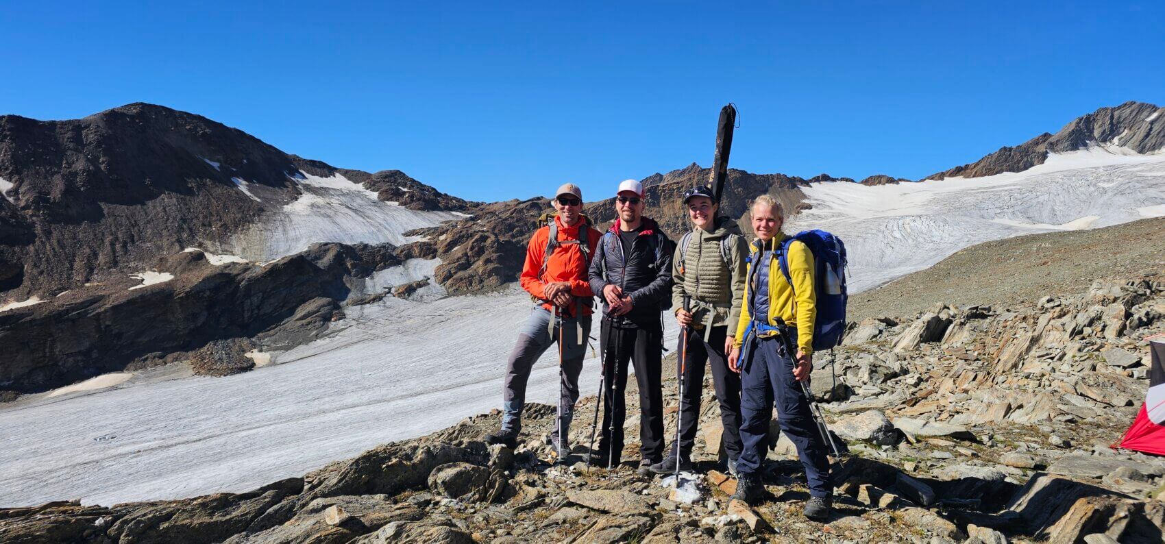 Eine Gruppe aus vier Personen auf einem Berggipfel bzw. Gletscher vor blauem Himmel