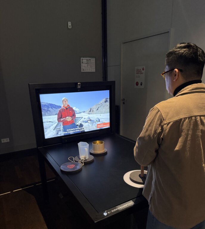 Eine Person steht vor der "Gesten"-Station in der Ausstellung "On Water. WasserWissen in Berlin" und betrachtet ein Video, das dort gezeigt wird