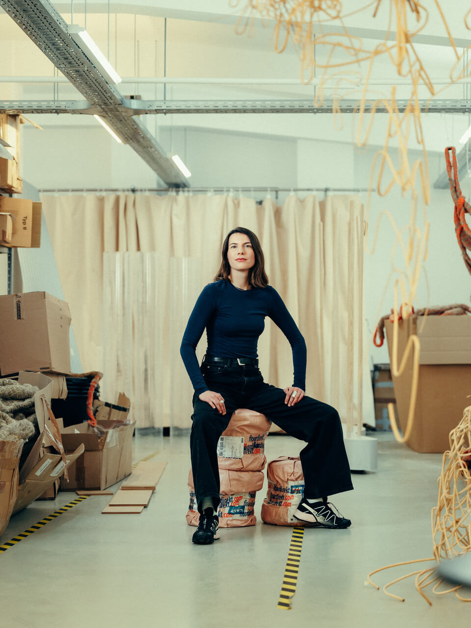 Porträt der Designerin und Taucherin Rasa Weber in einem hellen Atelierraum. Die Person sitzt zentral im Bild, um sie herum erkennt man verschiedene Materialien und Gegenstände.